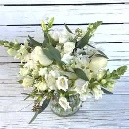 White flower arrangement with roses, hydrangea, and snapdragons in a clear glass vase