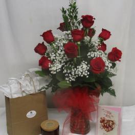 Red roses arranged in a glass vase with baby's breath and gift items nearby