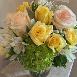 Bouquet of yellow and blush roses with white alstroemeria in a glass vase