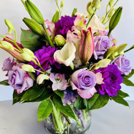 Bouquet of purple roses, lilies, and calla lilies in a glass vase