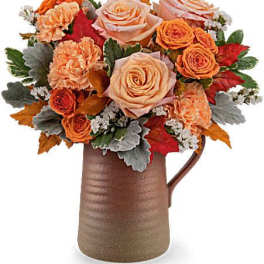 Orange and peach roses arranged in a brown pitcher vase