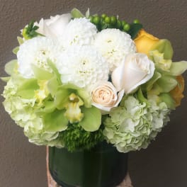 White and green floral arrangement with roses and orchids in a dark vase