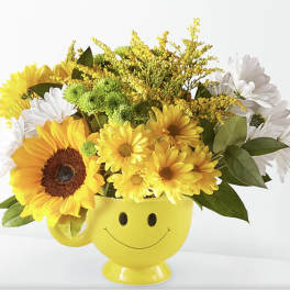 Yellow smiley-face mug filled with sunflowers and white daisies