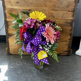 Mixed bouquet in a glass vase with a purple polka-dot ribbon