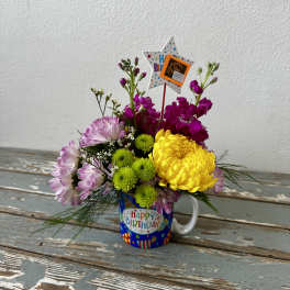 Birthday flower arrangement in a mug with pink, yellow, and green blooms