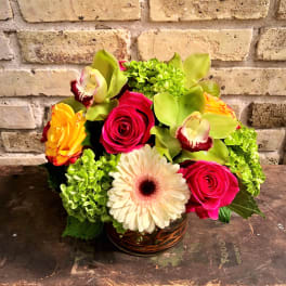 Bright mixed bouquet in a glass vase with roses, orchids, and a gerbera daisy