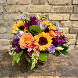Mixed bouquet with sunflowers, roses, and purple blooms in a low arrangement