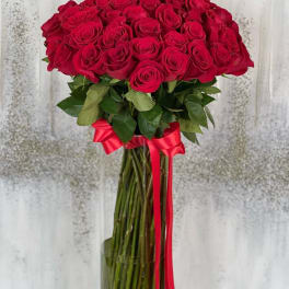 Tall bouquet of red roses in a glass vase with a red ribbon