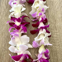 Garland of purple, pink, and white orchid blossoms on a wood surface