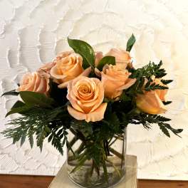 Peach roses arranged in a clear glass vase with greenery