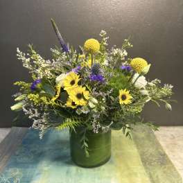 Mixed bouquet with yellow sunflowers and purple accents in a green vase