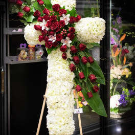 Large cross-shaped floral tribute with white blooms and red roses on an easel