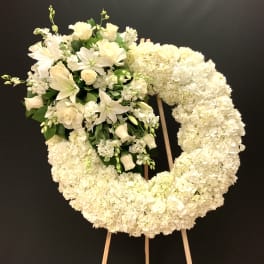 White floral wreath on an easel with a cluster of lilies and roses
