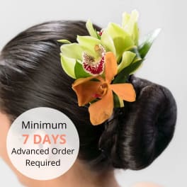 Orchid hairpiece with green and orange blooms pinned to a sleek dark hair bun