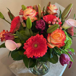 Mixed bouquet of pink, coral, and red flowers in a glass vase