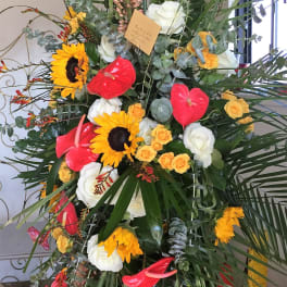 Tall floral standing spray with sunflowers, roses, and red anthuriums