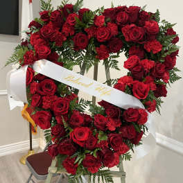 Heart-shaped red rose wreath with a white ribbon reading "Beloved Wife"