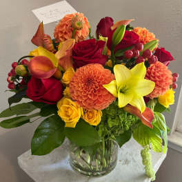 Mixed bouquet of red, orange, and yellow flowers in a clear glass vase