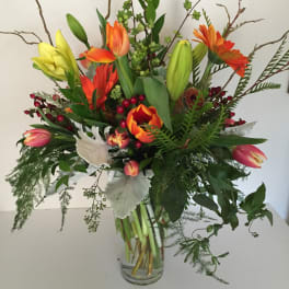 Tall mixed bouquet with tulips, lilies, and orange daisies in a glass vase