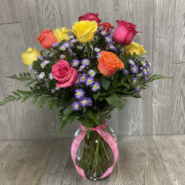 Mixed bouquet of colorful roses and purple daisies in a glass vase