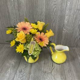 Yellow and peach floral arrangement in a yellow vase beside a matching pitcher
