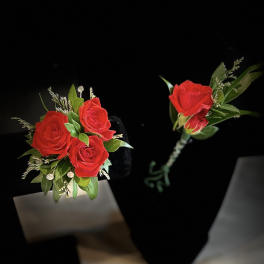 Red rose boutonniere with green foliage on a black background