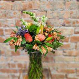 Mixed bouquet in a glass vase with coral, peach, purple, and white blooms