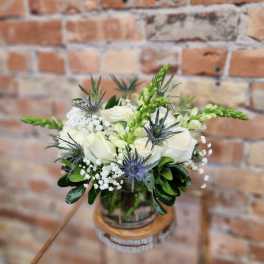 White rose bouquet with blue thistle in a glass vase