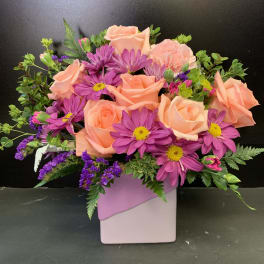 Peach roses and purple daisies in a pink square vase