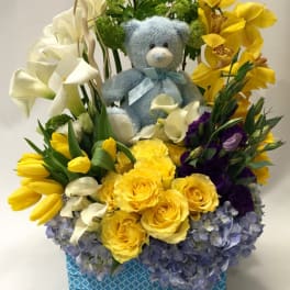 Flower arrangement with a teddy bear, yellow roses, calla lilies, and orchids