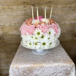 Pink and white flower cake on a pedestal stand with candles