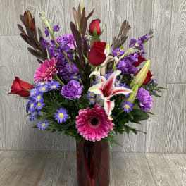 Mixed bouquet of red roses, lilies, and purple flowers in a red glass vase