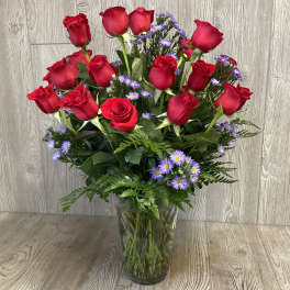 Red roses and purple daisies arranged in a clear glass vase