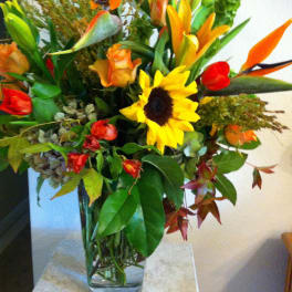 Mixed bouquet with sunflowers, lilies, and orange roses in a glass vase