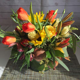Bouquet of orange tulips, yellow sunflowers, and lilies in a low arrangement