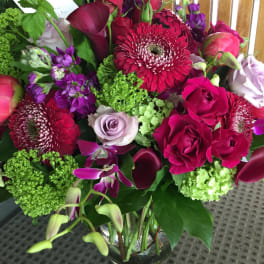 Mixed bouquet of pink, purple, and green flowers in a glass vase