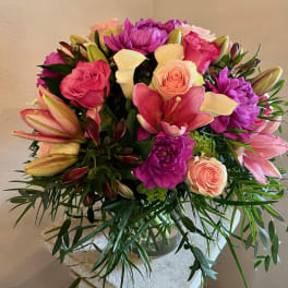 Mixed bouquet of pink lilies, roses, calla lilies, and purple blooms in a glass vase