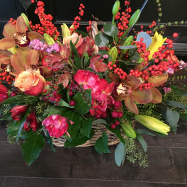 Basket arrangement of roses, orchids, lilies, and red berry stems