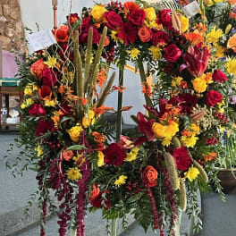 Large standing floral wreath with red, yellow, and orange blooms