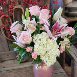 Pink and white bouquet with roses, lilies, carnations, and hydrangeas in a pink vase.