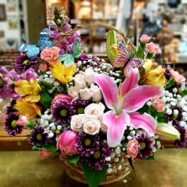 Basket arrangement of pink lilies, roses, and purple daisies with butterfly picks