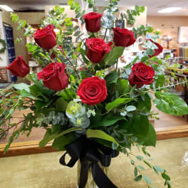Red roses in a clear glass vase with greenery and a black ribbon