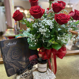 Red roses arranged with baby's breath, a chocolate box, and a candle