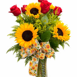 Bouquet of red roses and yellow sunflowers in a glass vase with a patterned ribbon
