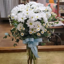 White daisy bouquet in a clear glass vase with a blue striped ribbon