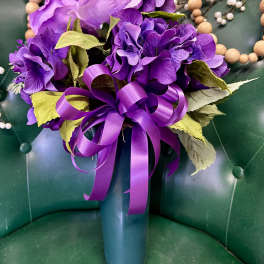 Purple floral arrangement in a teal vase with a ribbon bow
