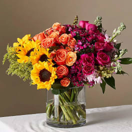 Mixed bouquet of sunflowers, roses, and pink flowers in a glass vase