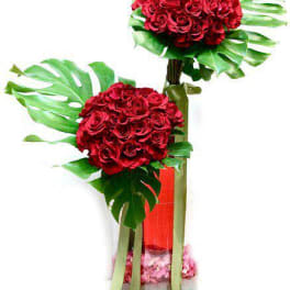 Tall modern arrangement of red roses in two spheres with large tropical leaves in a glass vase