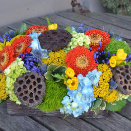 Low floral arrangement with red, yellow, blue, and green blooms in a wooden container