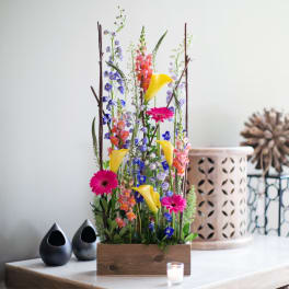 Tall mixed flower arrangement in a wooden box with yellow calla lilies and pink gerberas
